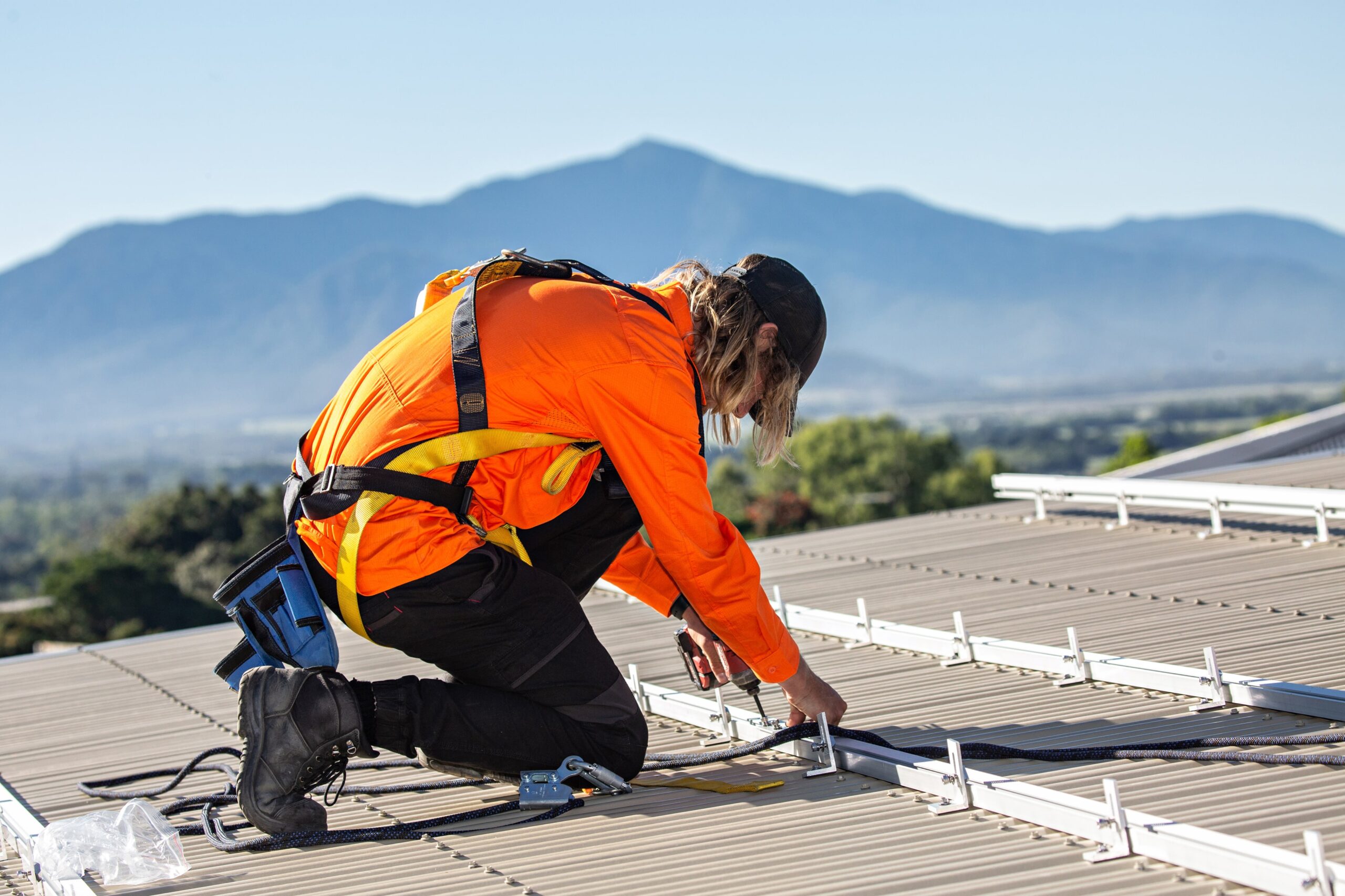 A man working on a roof installing solar panels with mountains in the background.