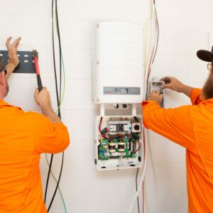 Two men in orange shirts working on a solar power electrical system.