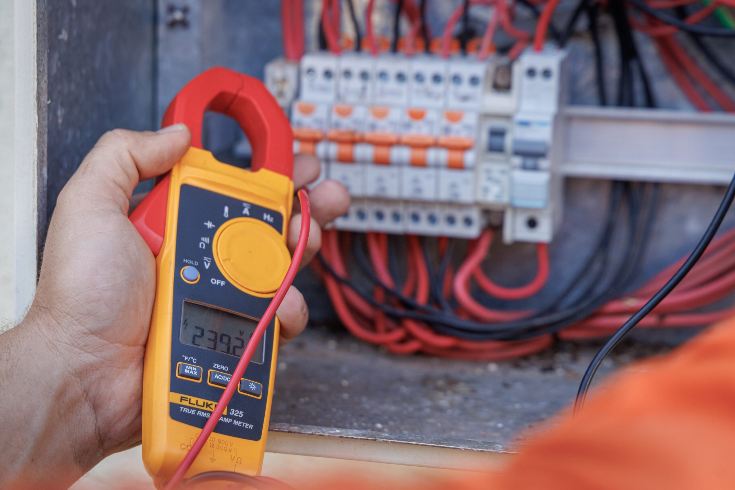 A person from Hielscher Electrical, in Cairns, holding a multimeter in front of an electrical panel.