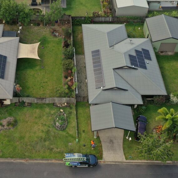 Aerial view of two Cairns homes with solar panels, green lawns, tropical trees, a driveway, and a vehicle with ladders outside.